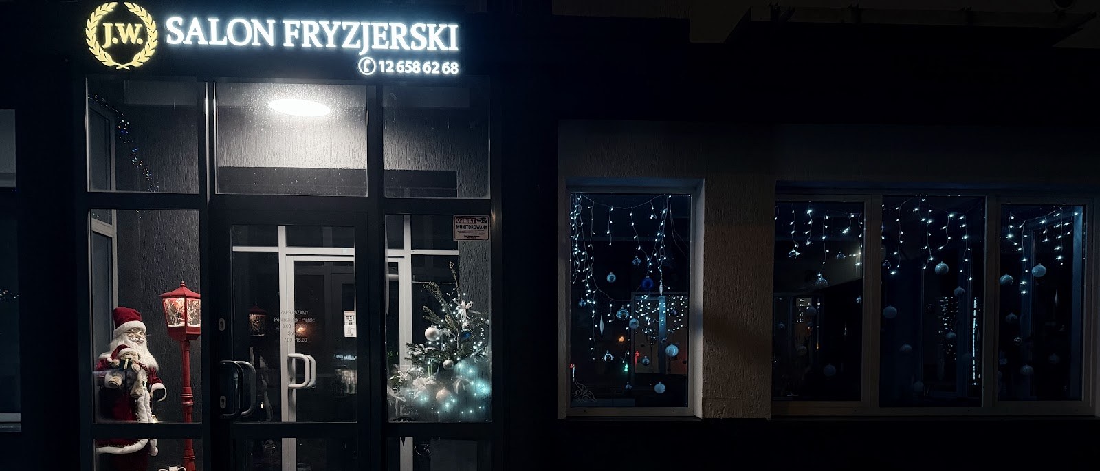 Podświetlony szyld i witryna salonu fryzjerskiego J.W. wieczorem